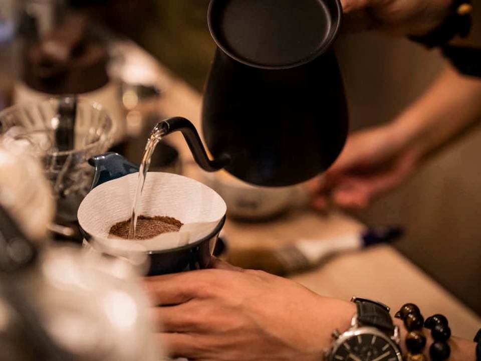 有一雙手拿著茶壺正在沖咖啡,一道水柱正注入咖啡粉中